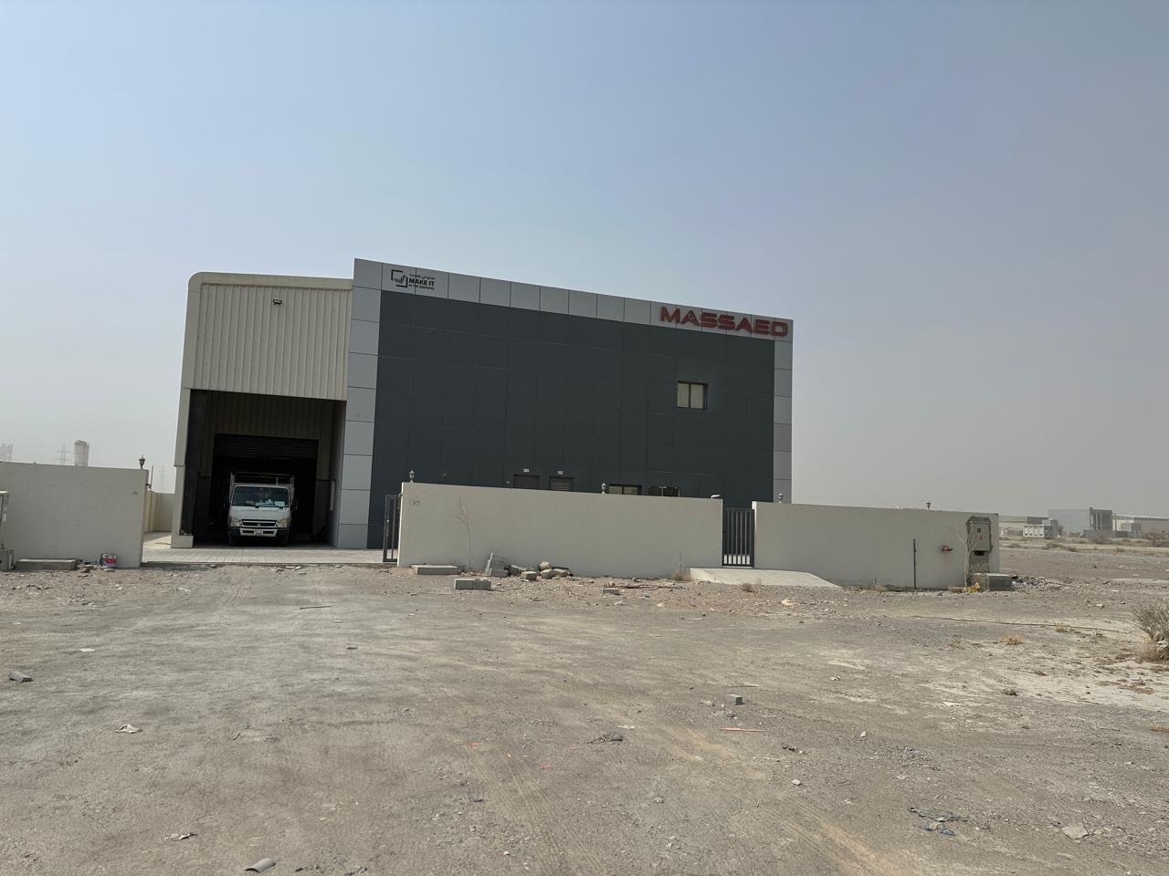 Wide exterior view of the MASSAED factory building in Ras Al Khaimah with perimeter wall and loading entrance